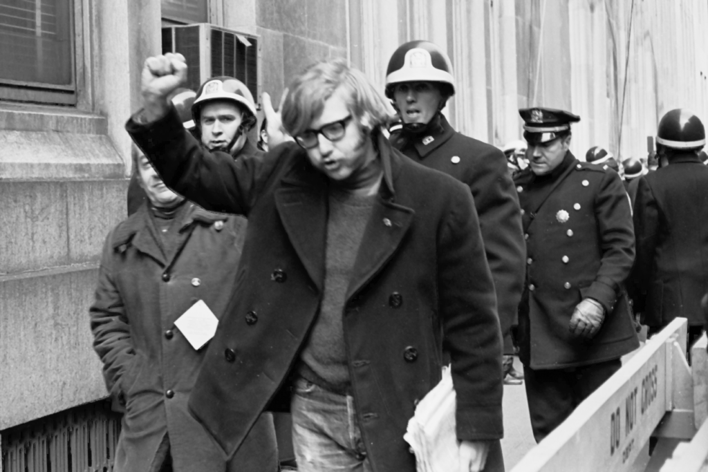 Man giving power sign behind Police barricade